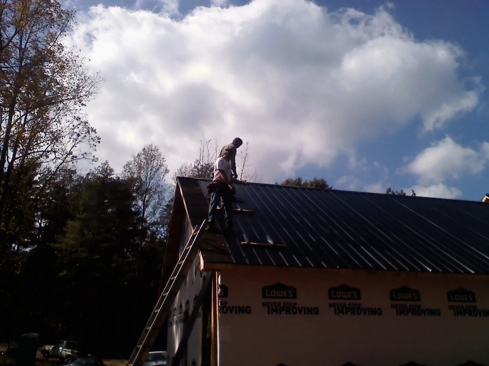Roofer fastening dark metal panels high against a cloudy sky, from a Roof Inspection job in Benson