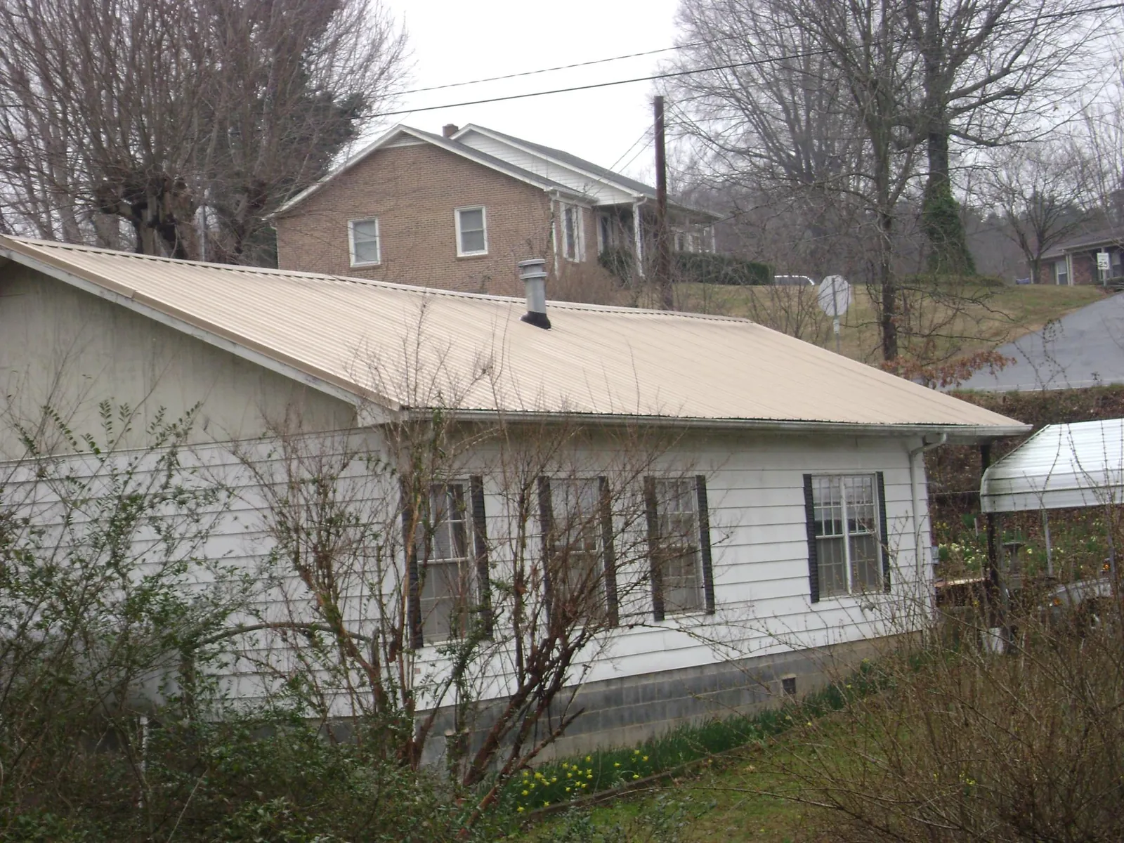 Tan metal roof on a white sided house set into a hillside — Commercial Roofing by Roofing Brothers in Benson